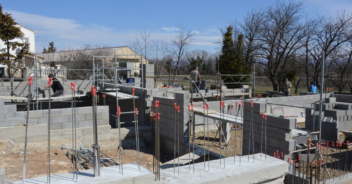 Sunlit construction site with workers on concrete foundation under a clear blue sky.